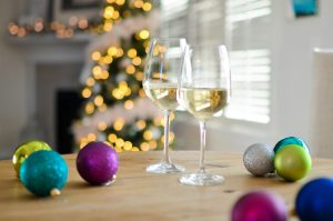 wine classes on a table surrounded by holiday bulbs and a tree lit by golden-white lights left out of focus in the background.